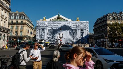 Des personnes marchent devant une installation de l'artiste français JR représentant une caverne qui couvre une partie de la façade de l'Opéra Garnier pendant sa rénovation dans le centre de Paris, le 7 septembre 2023. (DIMITAR DILKOFF / AFP)