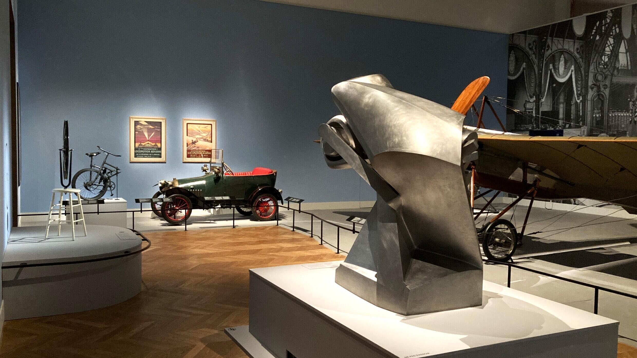 L’aéroplane d’Alain Deperdussin de 1911 en face d’une roue de bicyclette de 1913 de Marcel Duchamp dans l’exposition « Le Paris de la modernité » au Petit Palais.